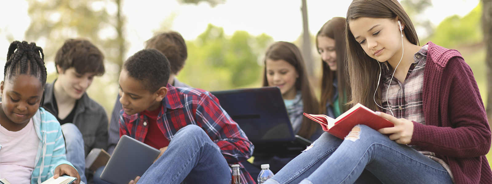 group of students sitting outdoors and reading, working on homework and interacting with each other.